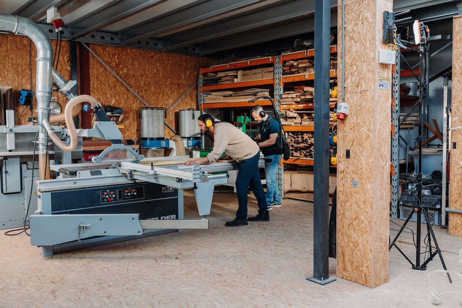 The open workshop floor, two makers at the sliding table saw