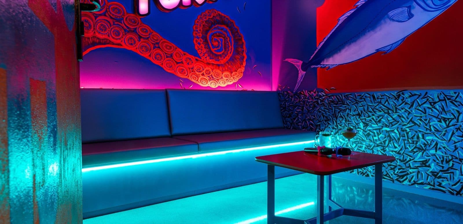 Karaoke booth with octopus mural, lit in pink and cyan